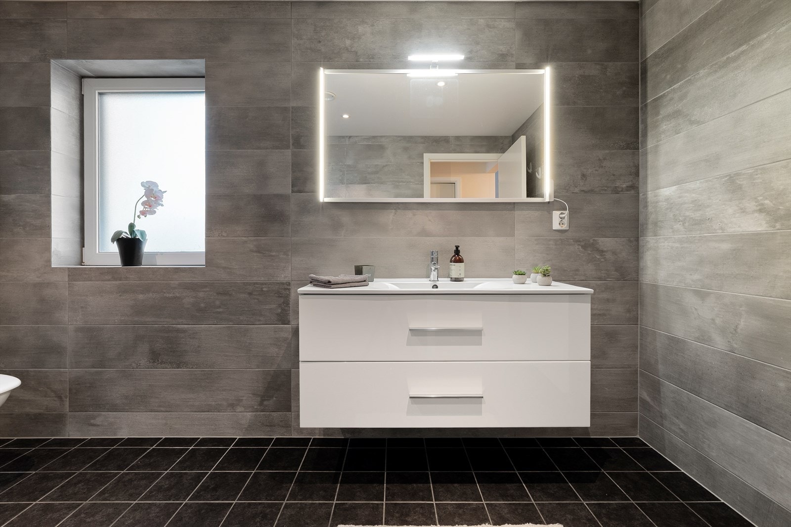 Stilrent bad med flislagte vegger og gulv, og malte plater i taket. Galleribilde