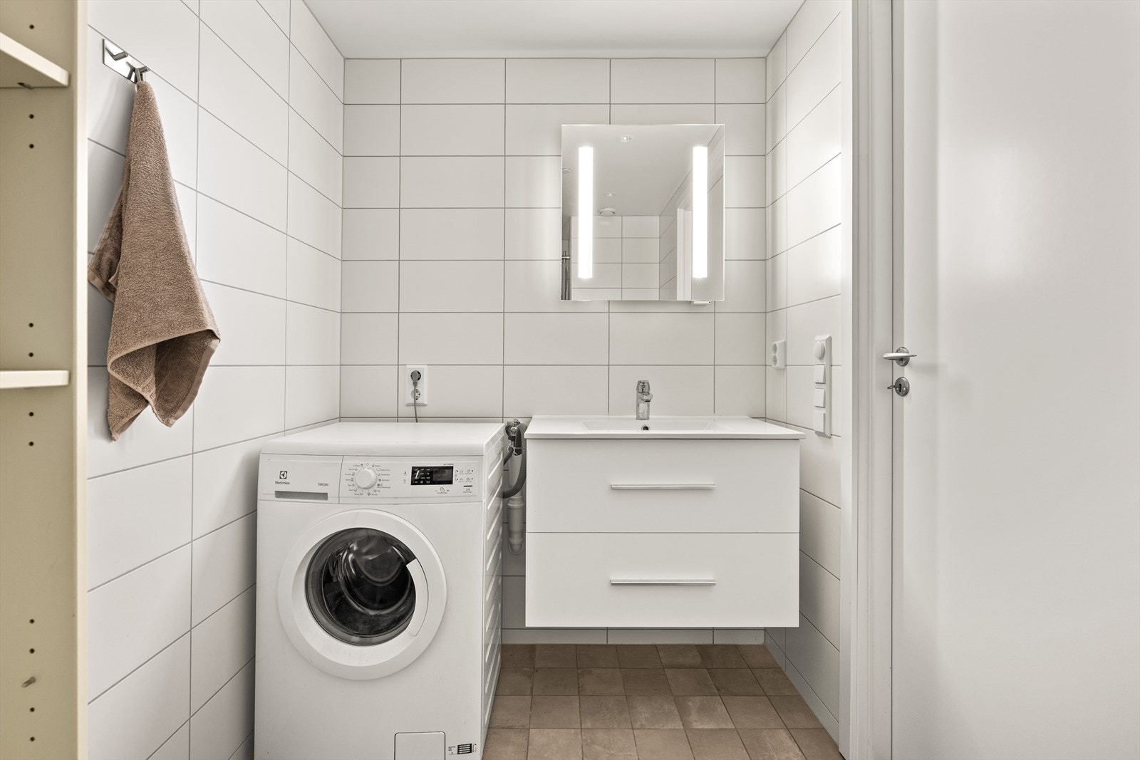 Badet har keramiske fliser på vegger og gulv. Servant i innredningen og opplegg til vaskemaskin. Galleribilde