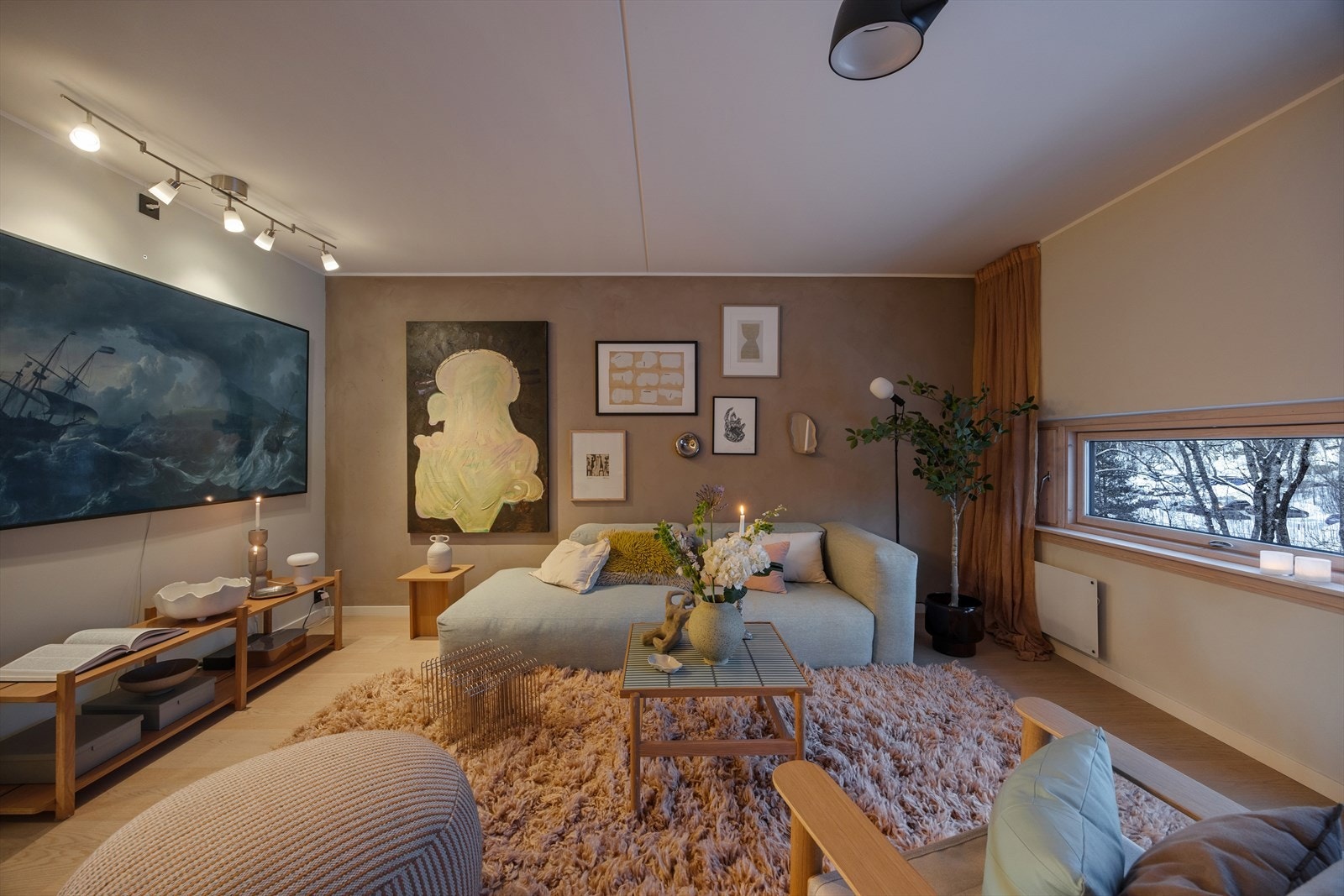 Den åpne stuen byr på en behagelig atmosfære, med gjennomtenkt belysning og utsikt over grønne omgivelser. Galleribilde