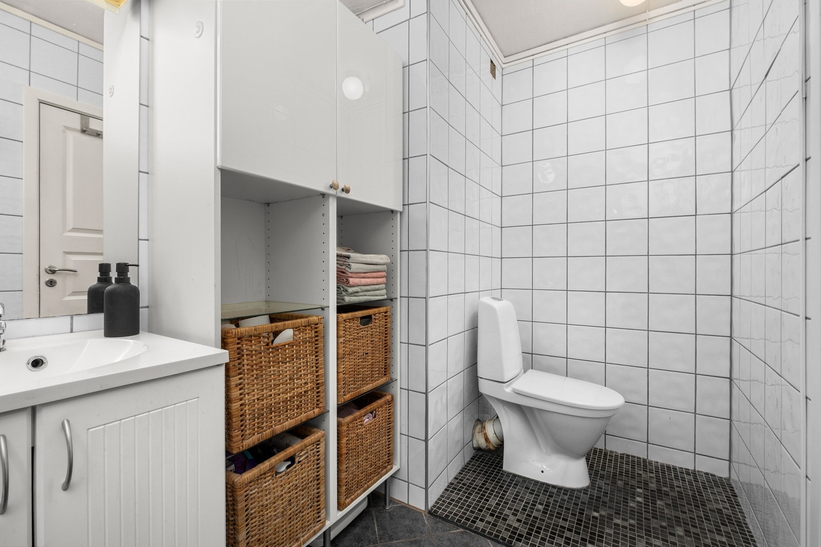 Badet er innredet gulvmontert toalett, veggmontert servantinnredning og speil med overlys, dusjkabinett og opplegg for vaskemaskin Galleribilde