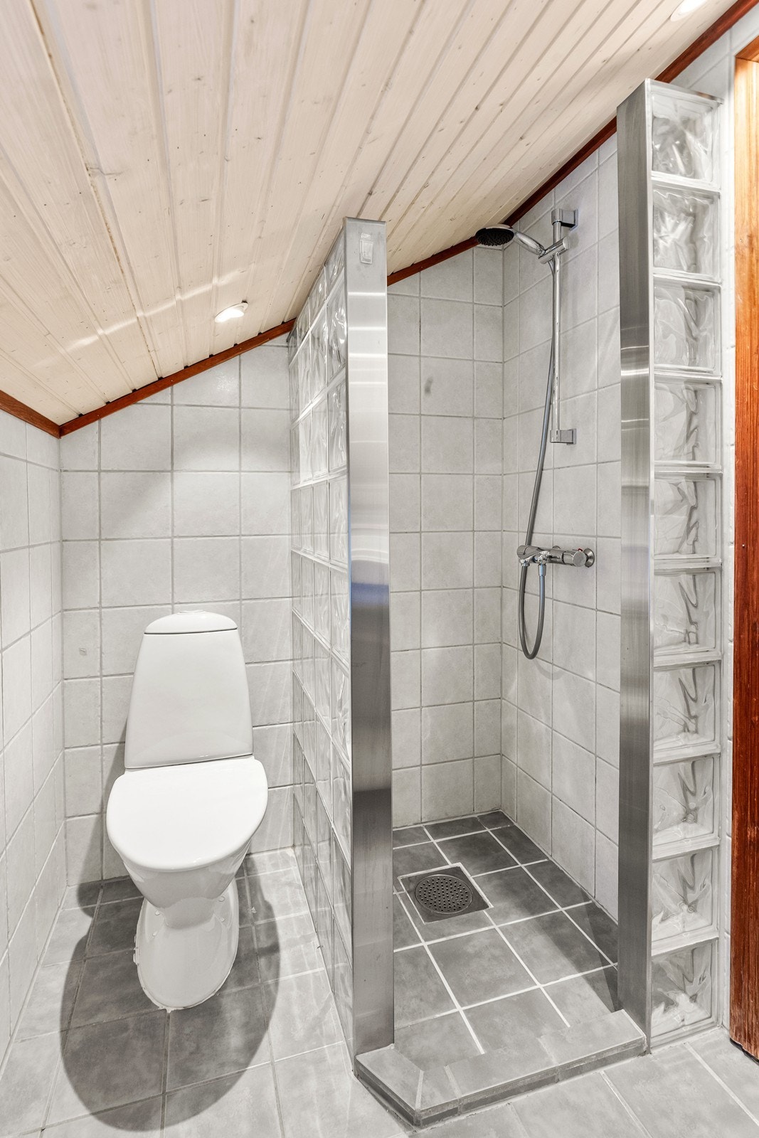 Dusjsonen er avskjermet med glassbyggerstein, og rommet har panel i taket. Galleribilde