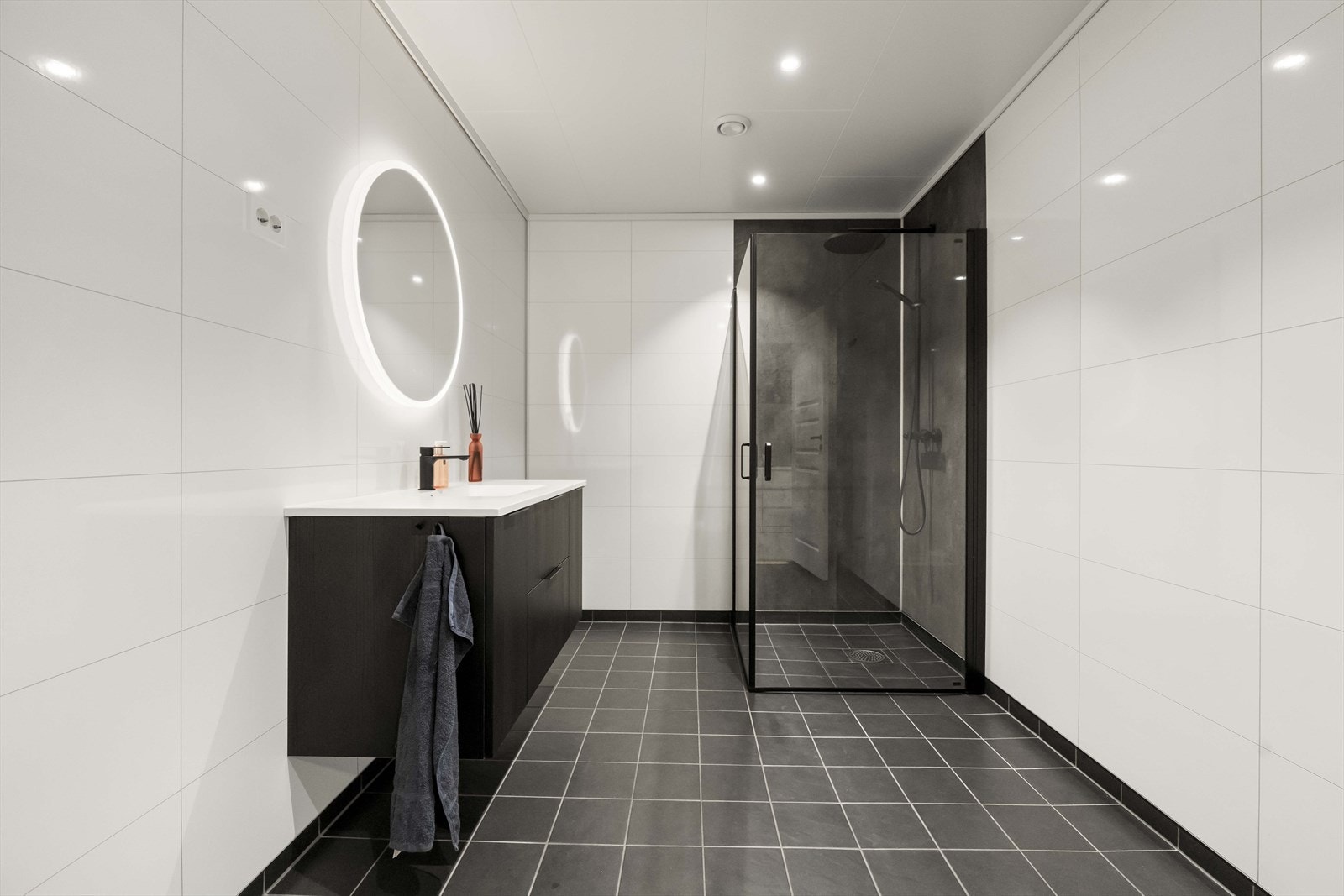 Badet har flislagt golv med varmekablar, mørk innredning og dusjhjørne Galleribilde