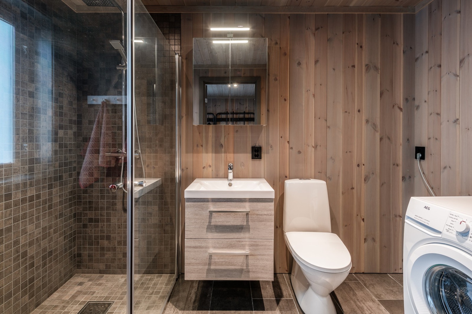 Lekkert bad med fliser på gulv og i dusjsone, beiset trepanel på tak og øvrige vegger Galleribilde