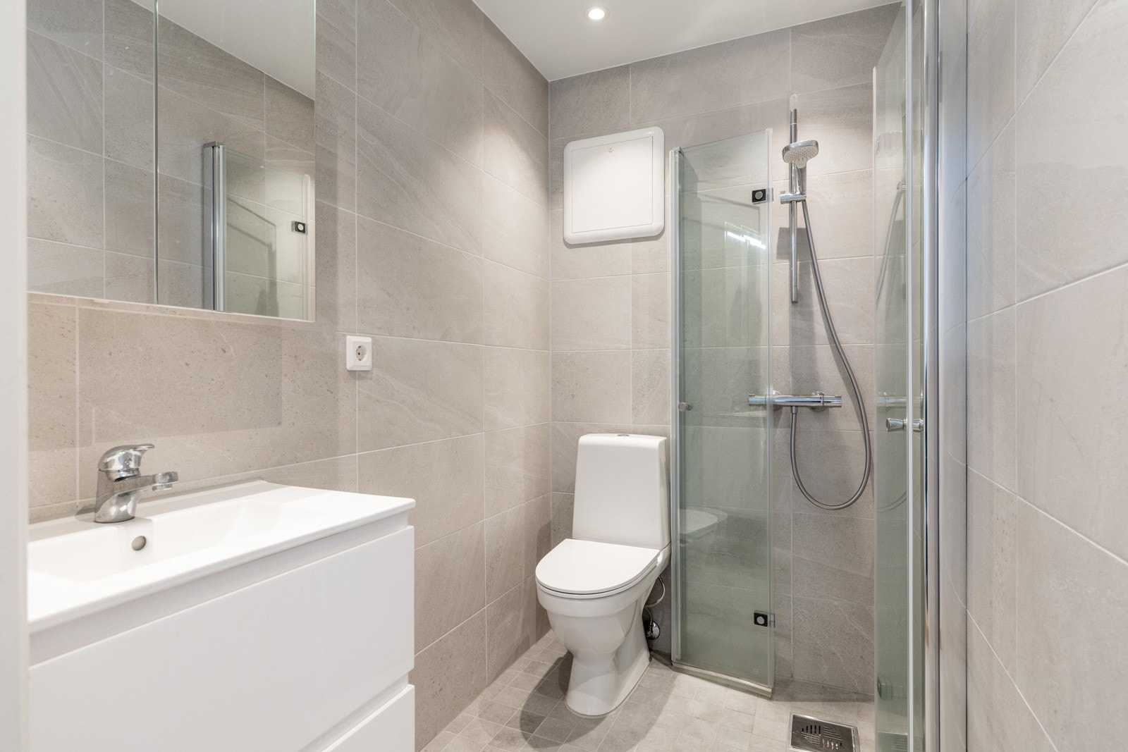 Innredningen på badet består av enkel servant, speilskap, toalett og dusjhjørne med svingbare glassdører Galleribilde