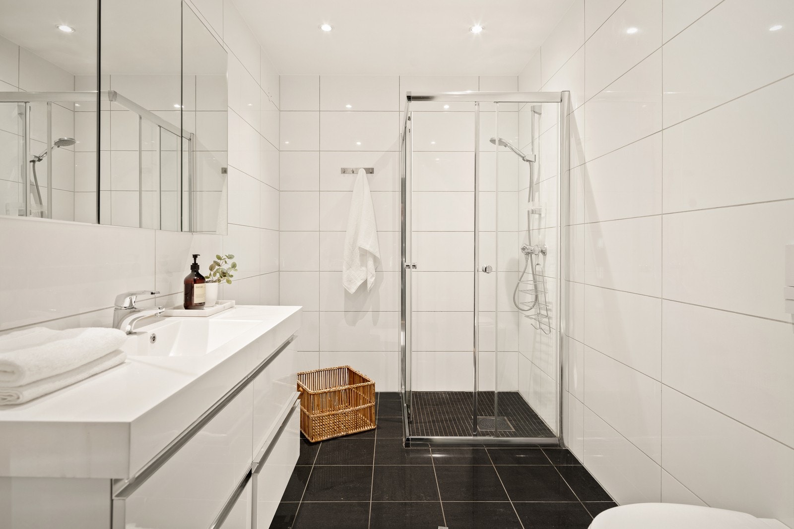 Tidløst bad som er innredet med servant nedfelt i baderomsinnredning, veggmontert toalett og dusjhjørne med dusjvegger. Galleribilde