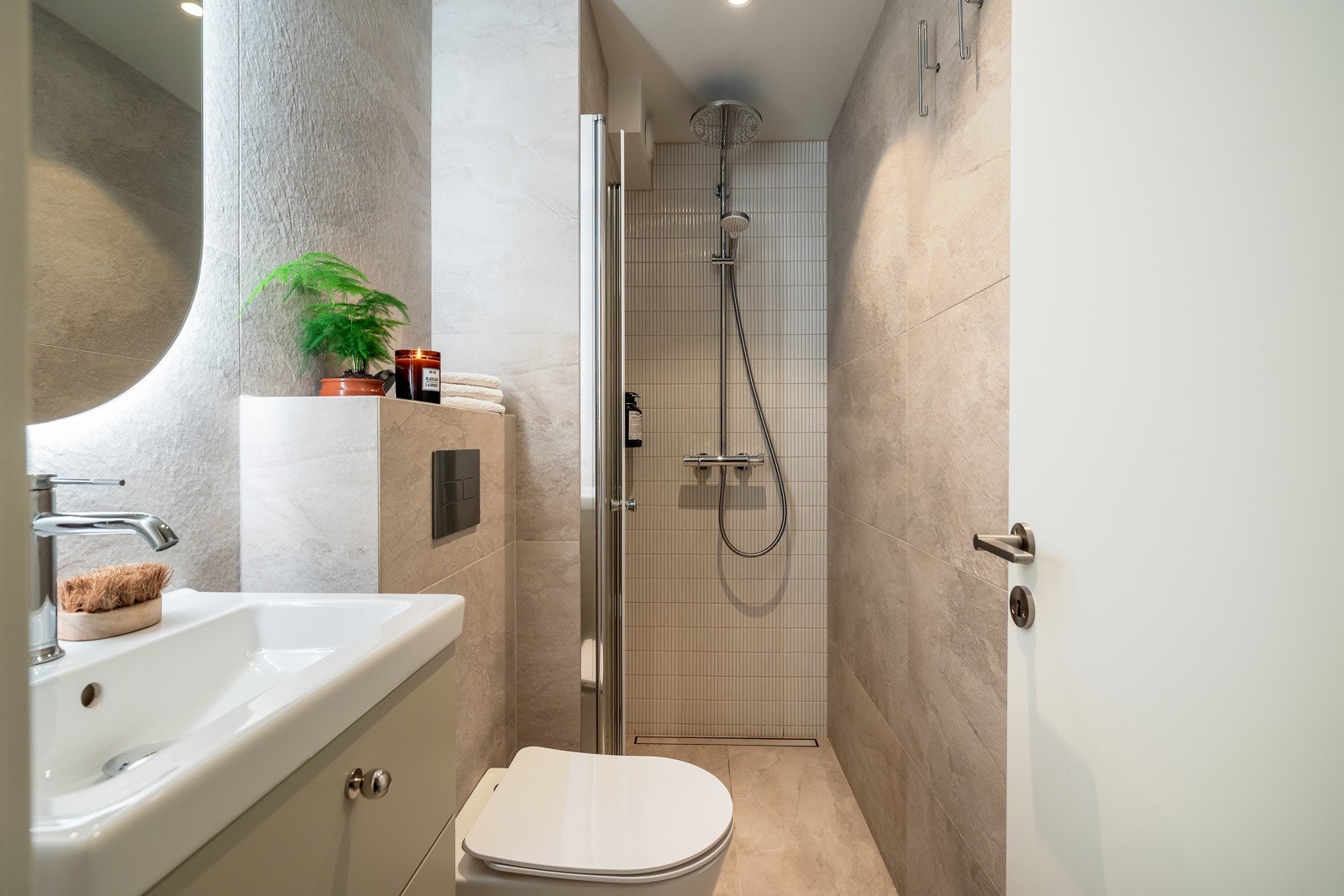 Badet er av god størrelse og er velutnyttet med bl.a heldekkende servant over skuffeseksjon og speil med integrert belysning, veggmontert toalett, dusjhjørne med foldedører i glass, samt håndholdt- og regnfallsdusj Galleribilde