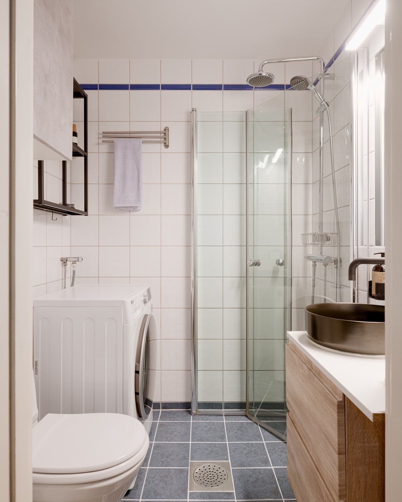 Videre har badet gulvstående toalett og dusjhjørne med glassdører og to-greps armatur samt regnfalldusj. Det er opplegg for vaskemaskin. Galleribilde