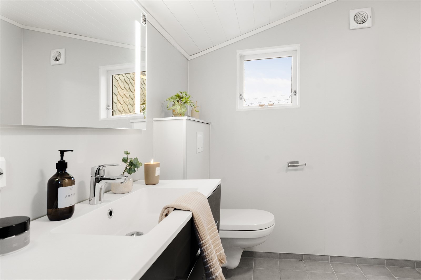 Rommet har fliser på gulv og våtromsplater på vegg. Rommet er innredet med dusjkabinett, seksjon med heldekkende vask, veggmontert toalett og opplegg for vaskemaskin. Galleribilde