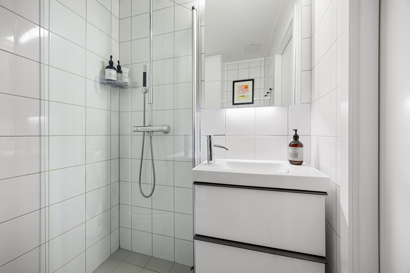 Badet er utstyrt med dusjhjørne, servant med underskap, speil og toalett Galleribilde