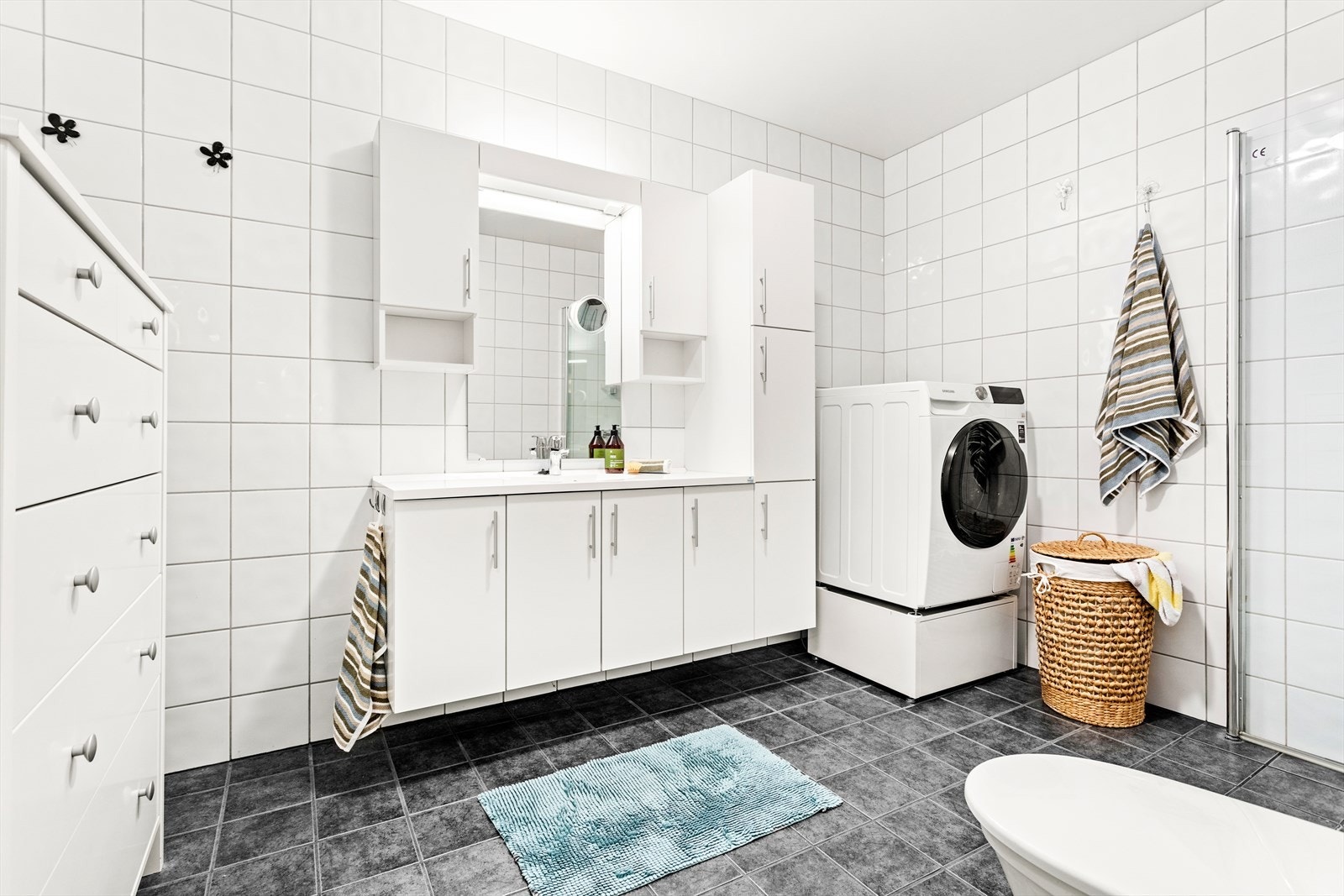 Badet er utstyrt med vassboren golvvarme, dusjhjørne med innfellbare glasdører, benkeskåp med nedfelt servant, spegel med lyslist, balansert ventilasjon og toalett. Galleribilde