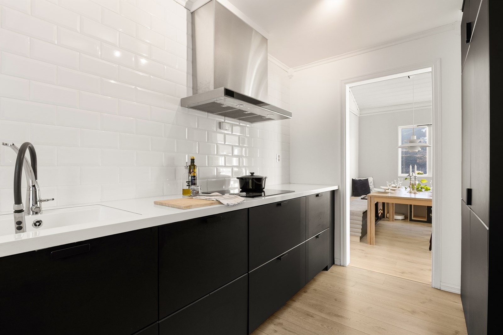 Kjøkkenet er innredet med glatte fronter i mørke fargetoner og hvit benkeplate i laminat. Galleribilde