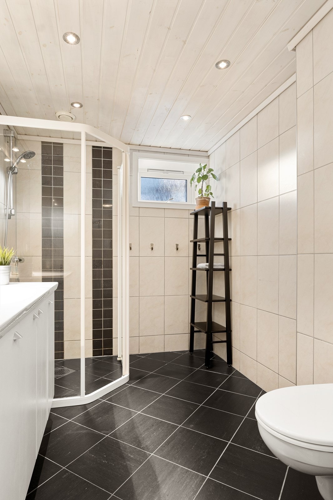 Badet er innredet med dusjvegg, servant med møblement og veggmontert toalett. Galleribilde