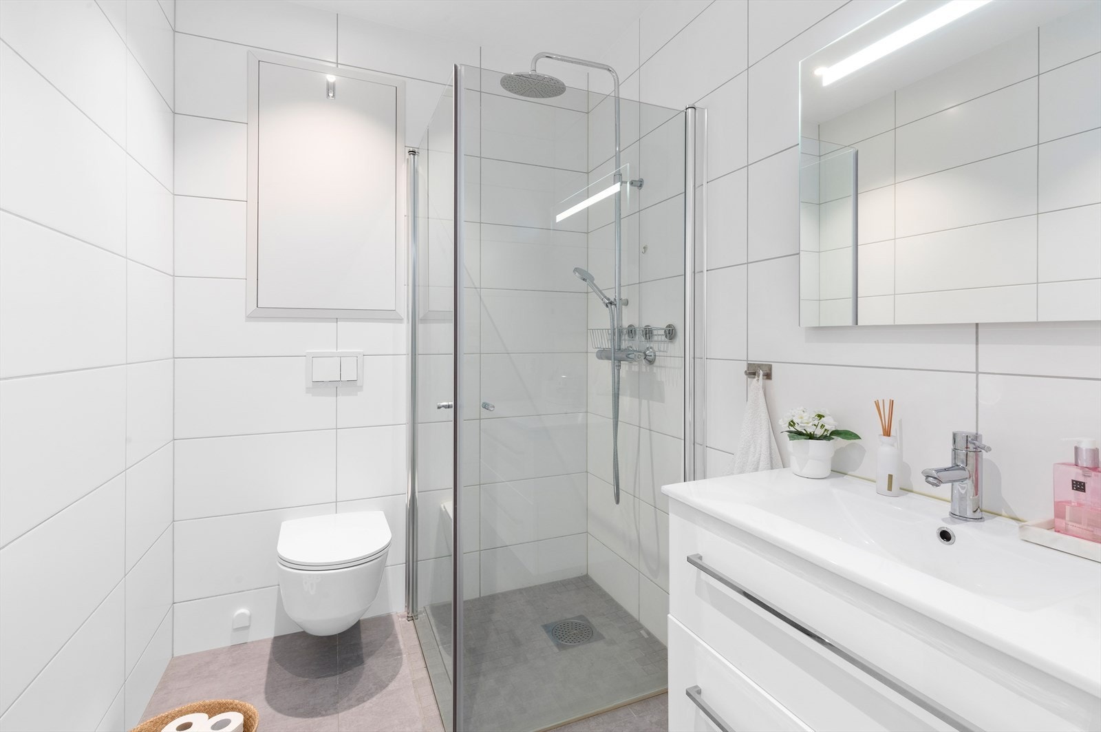 Flott flislagt bad med dusjhjørne, vegghengt toalett og servant med underskuffer. Galleribilde