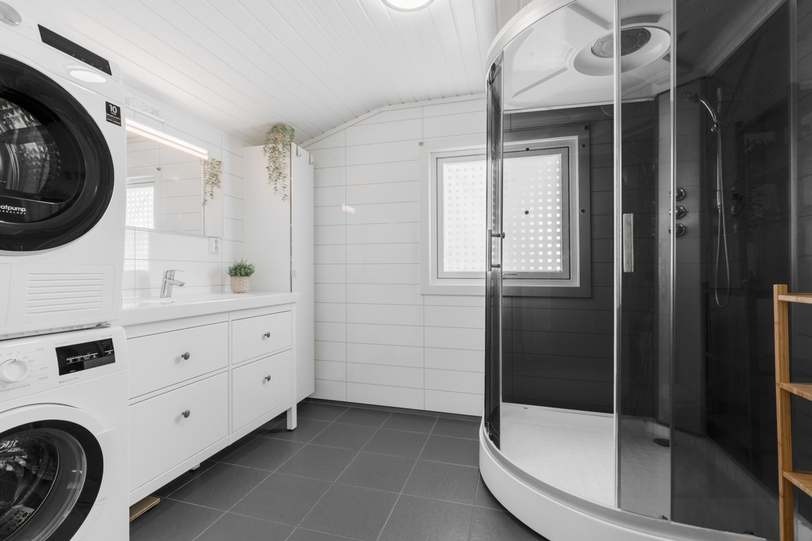 Delikat baderom bestående av servant med underskuffer, dusjkabinett, gulvstående toalett og opplegg til vaskemaskin Galleribilde