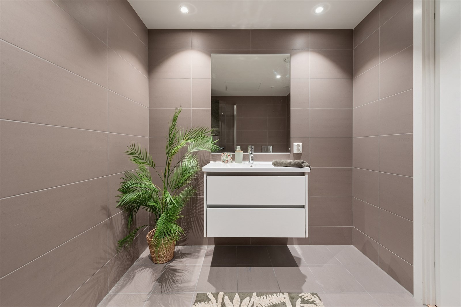 Rommet har moderne servantskap med høyglansfronter, vegghengt toalett og et praktisk nedsenket dusjhjørne med svingdører. Galleribilde