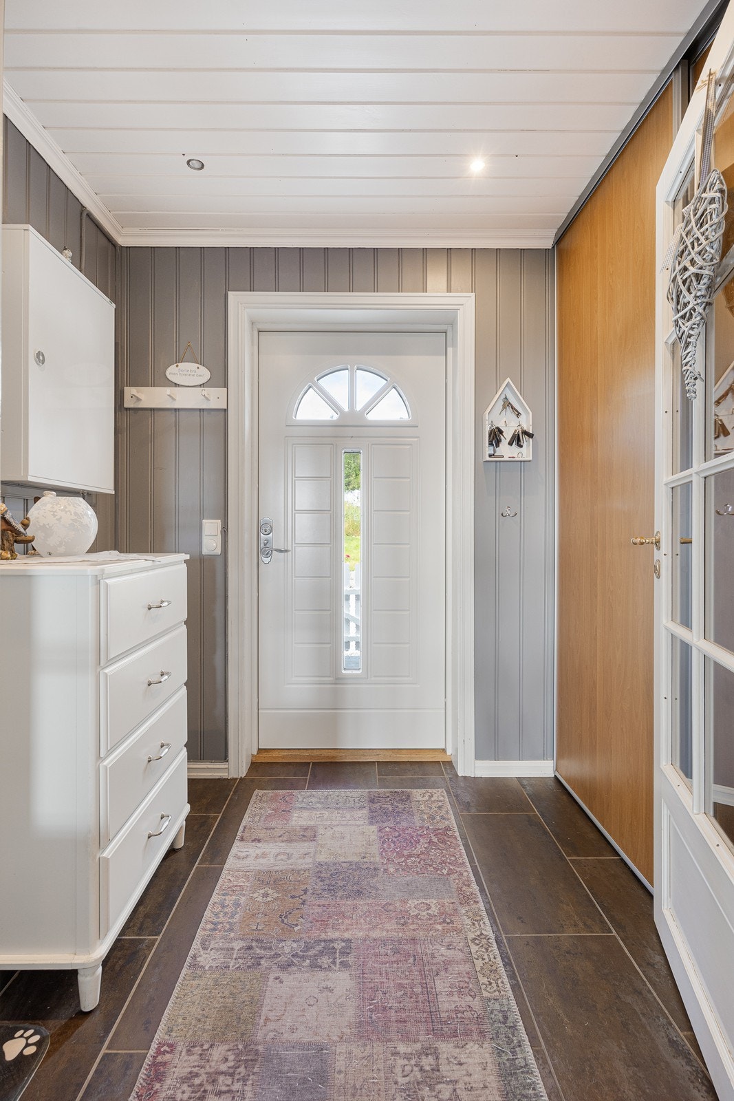 Entreen har gråmalt panel på veggene, downlights i himlingen, grå fliser på gulv med gulvvarme samt en romslig, plassbygd skyvedørsgarderobe. Galleribilde