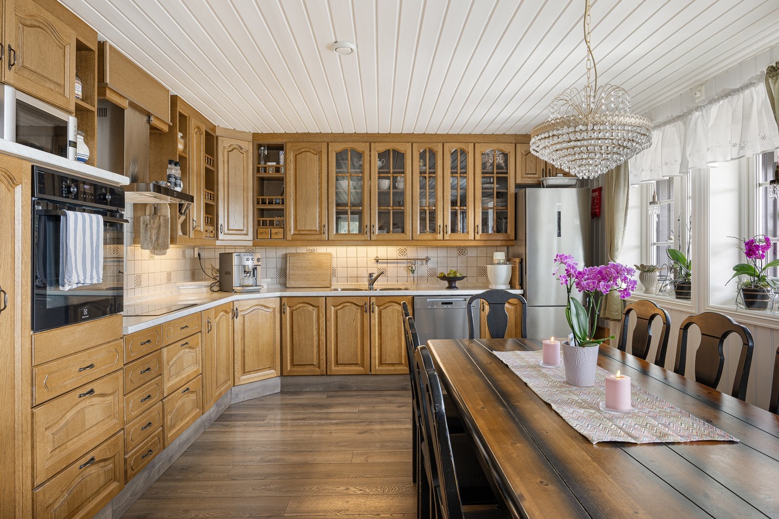 Kjøkkenet har et klassisk design med gode benkeflater og oppbevaringsplass. Innredningen har gylne, profilerte fronter, vitrinedører, takhøye skap og lys laminatbenkeplate med nedfelt kum i stål. Galleribilde