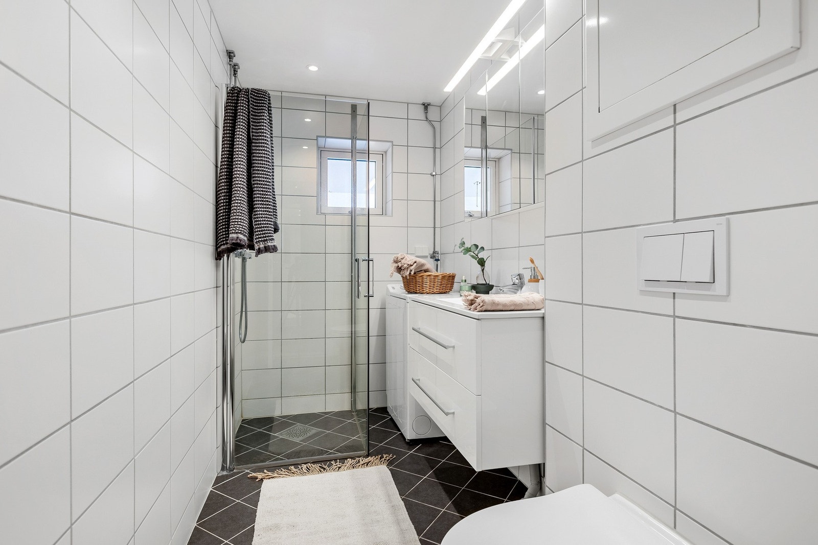 Bad med romslig dusjhjørne og glassvegger, gjennomgående fliser og god belysning. Galleribilde