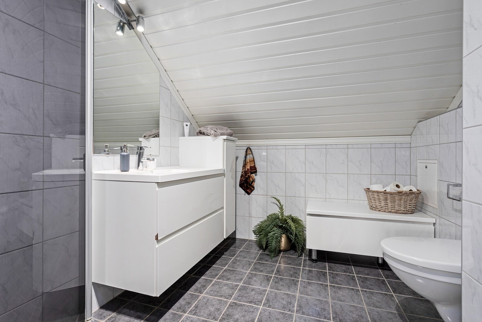 Badet er innreia med nedfelt servant, veggmontert toalett og dusjhjørne. Det er nytta flis på veggar og taket har panel. Golvet er flislagt og har elektriske varmekablar. Galleribilde