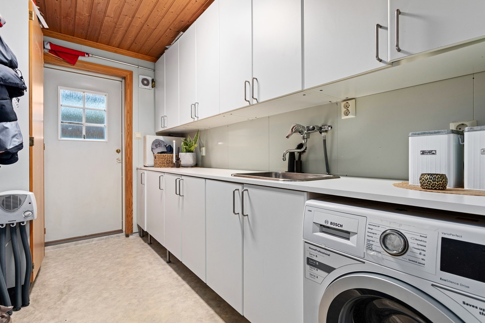 Vaskerommet har belegg på golv og plater på veggar. Innreiing består av benkeinnredning med vaskekum og overskåp, og opplegg for vaskemaskin. Frå rommet er det eigen utgang til tunet. Galleribilde