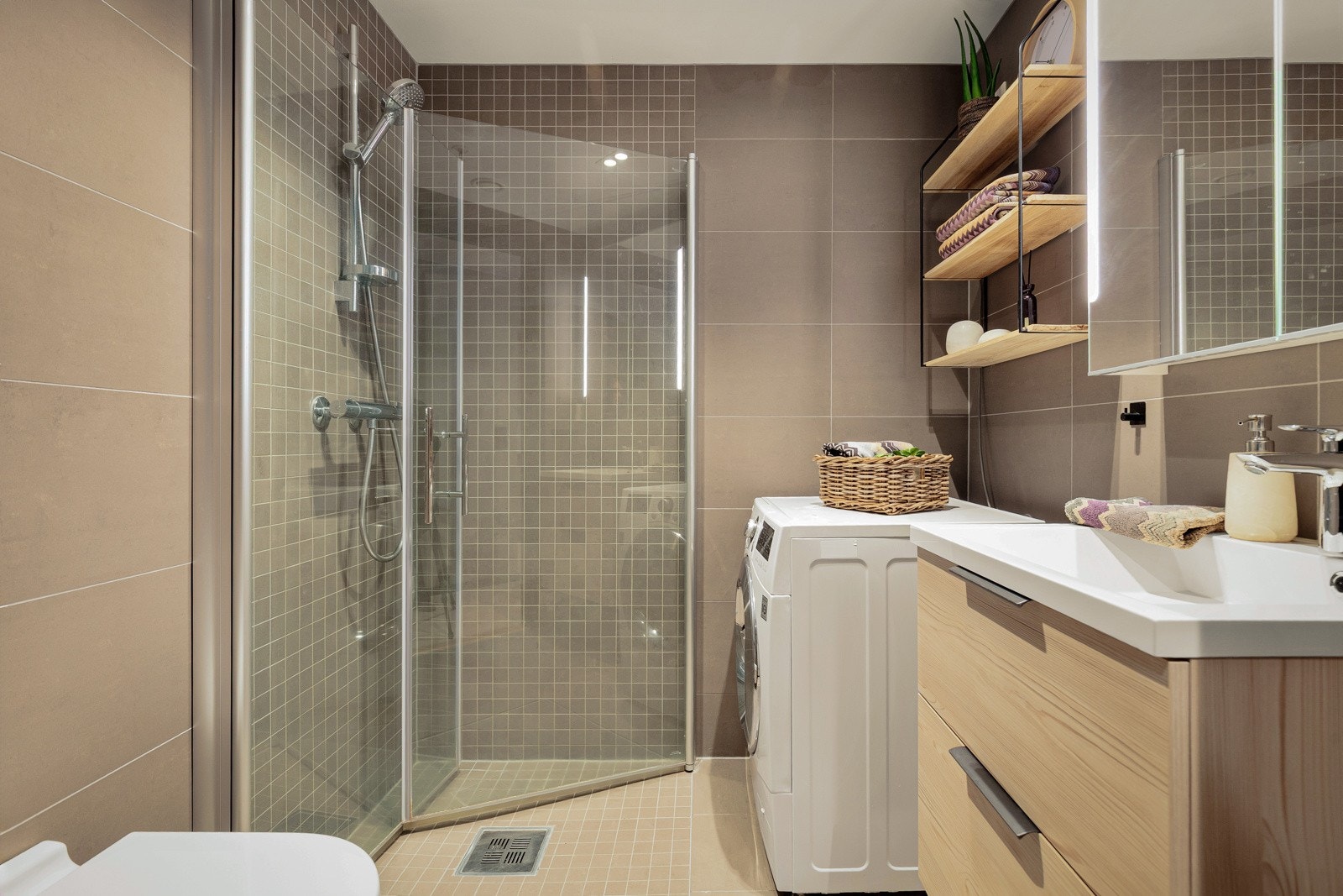 Lekkert baderom med veggmontert wc, dusj, servant og opplegg til vaskemaskin - dusjhjørne med innfellbare glassdører Galleribilde