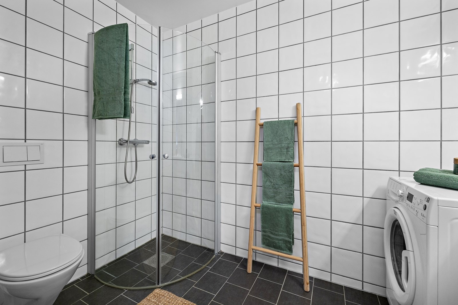 Badet er utstyrt med vegghengt toalett og et dusjhjørne med innfellbare glassdører. Galleribilde