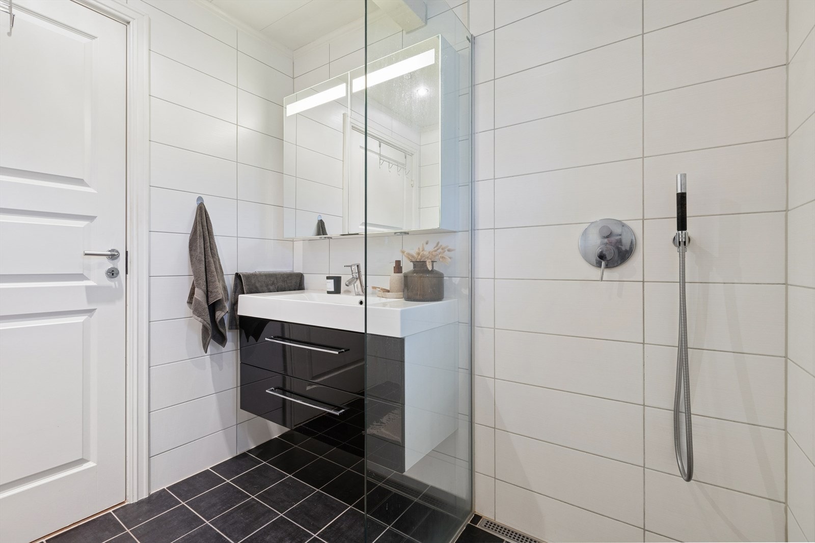 Badet har et stilrent design med hvite veggfliser, sorte gulvfliser og dusj med elegante glassvegger. Galleribilde