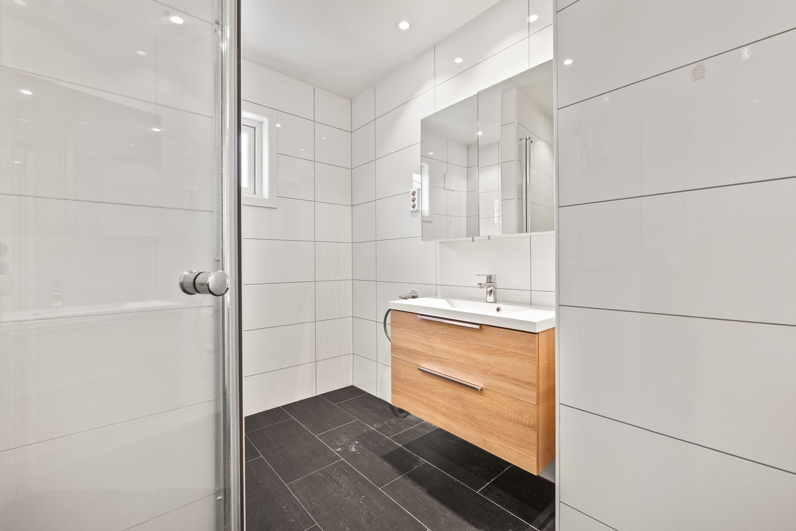 veggmontert toalett, helstøpt servant i innredning og dusjhjørne med glassdører. Det er avsatt plass og opplegg for vaskemaskin Galleribilde