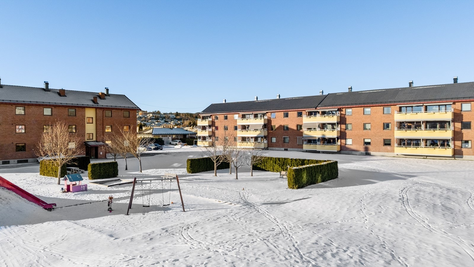 Tomten fremstår godt holdt, og mellom bebyggelsen er det en stor plen med sittegrupper til felles bruk og trivelig lekeplass med lekeapparater. Galleribilde