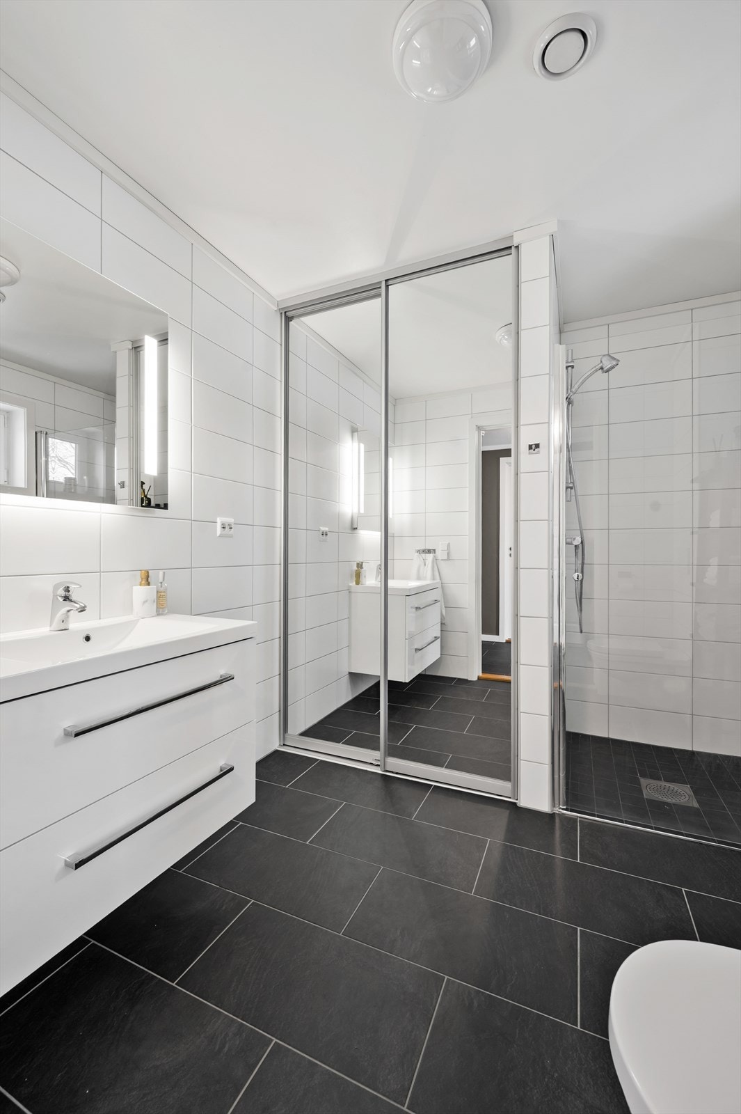 Pent flislagt baderom med skyvedører mot nisje hvor man kan ha vaskemaskin. Galleribilde