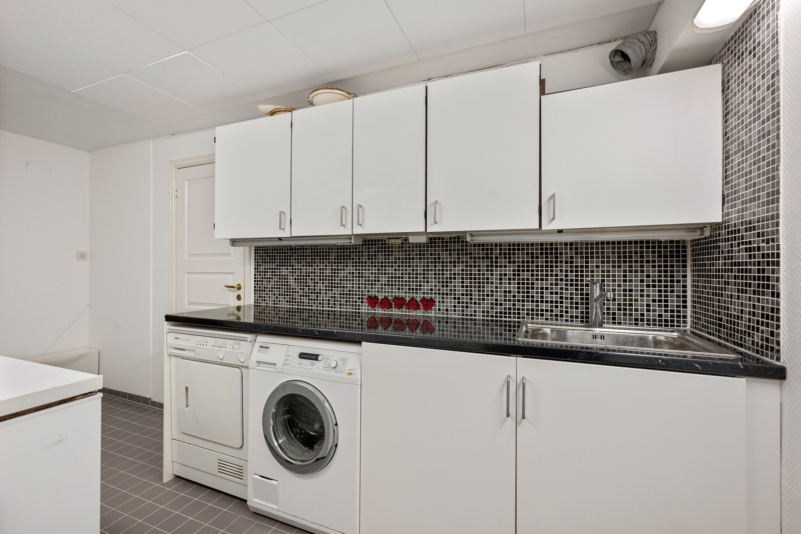 Vaskerommet er innredet med benkeplate med vask, underskap, nisje for vaskemaskin og tørketrommel, samt godt med oppbevaringsplass i overskap. Galleribilde