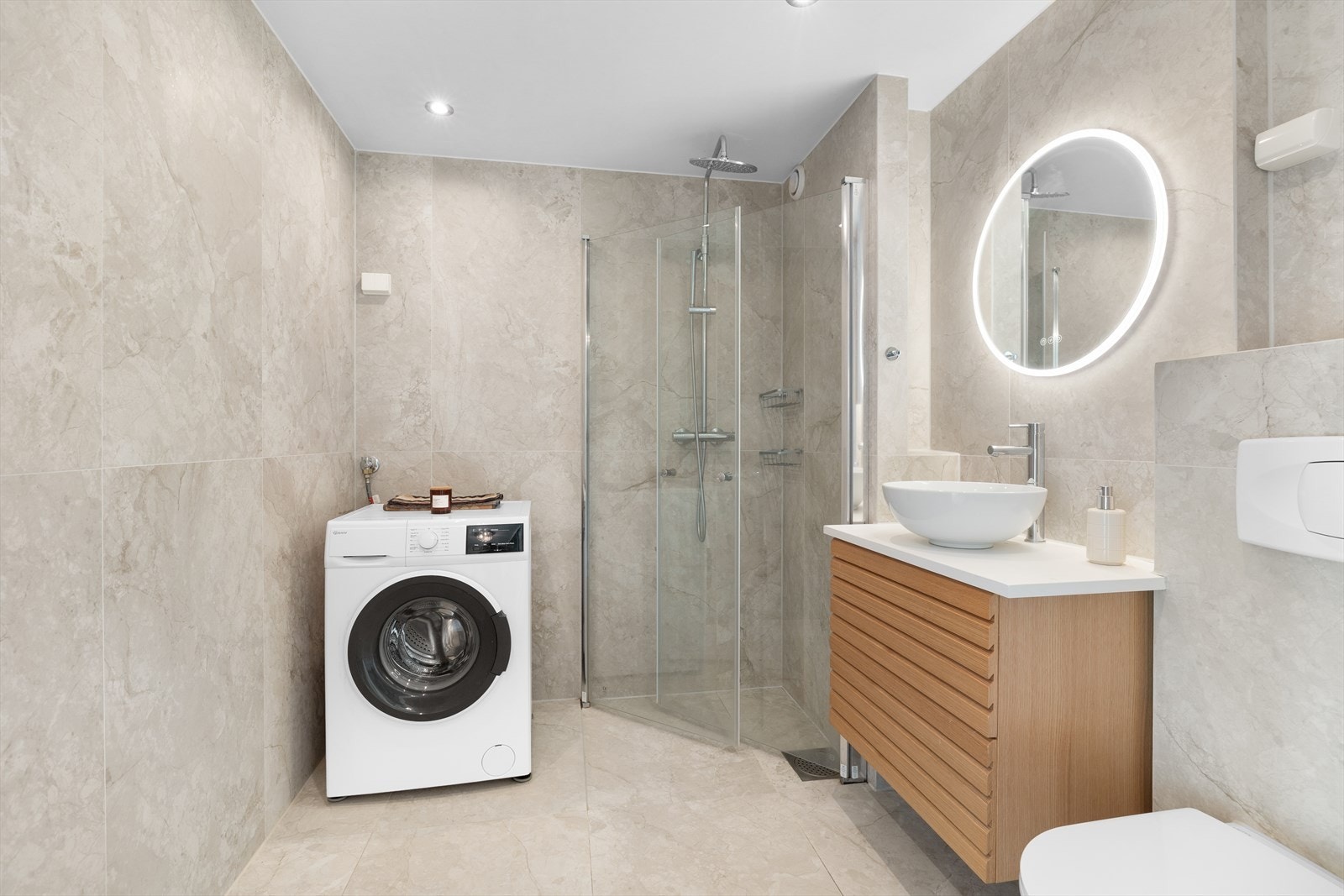 Innredningen fremstår med dusj, servant med underskap, speil med lys, wc og opplegg for vaskemaskin og tørketrommel. Galleribilde