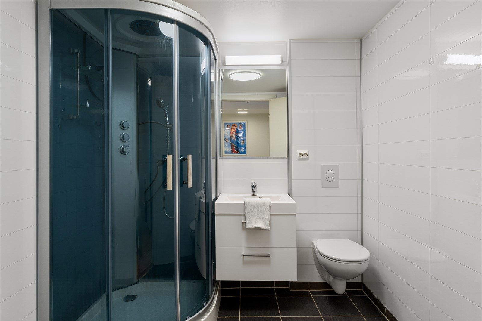 Bad med fliser på gulv og gulvvarme, innredet med vegghengt wc, dusjkabinett og seksjon med vask Galleribilde