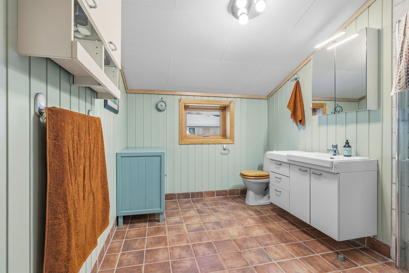 Badet er romslig og har panel på veggene og fliser på gulvet. Galleribilde