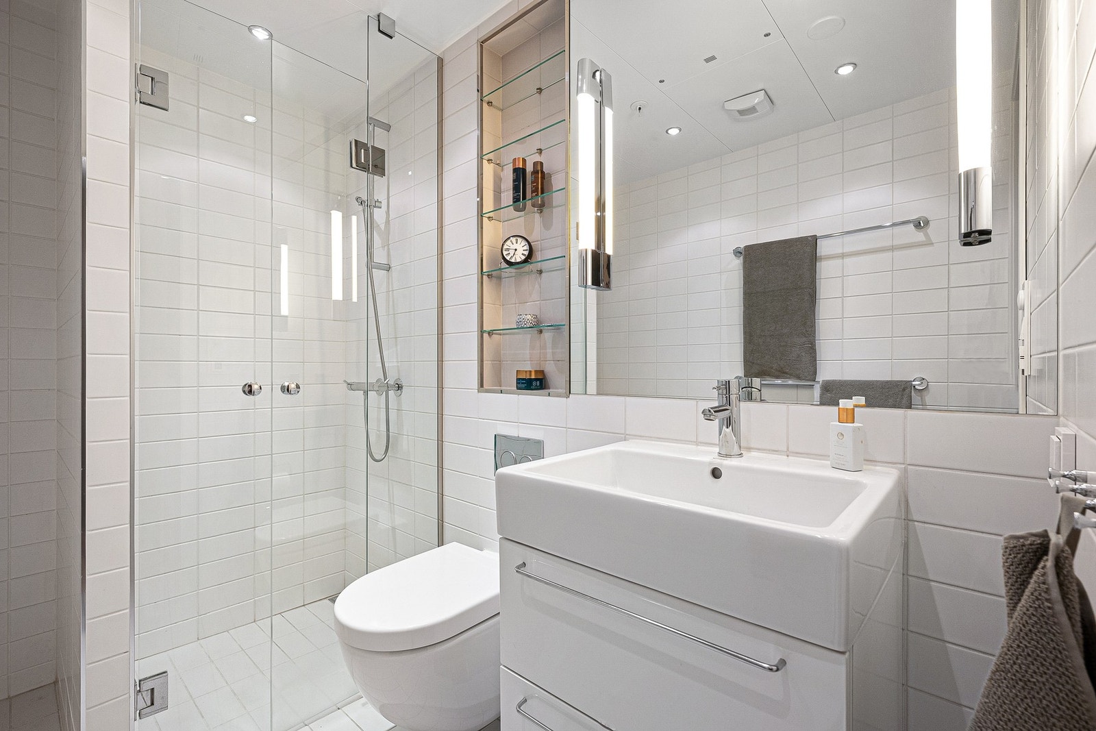 Moderne flislagt bad med stilren baderomsinnredning i benkeskap med glatte fronter, og innfliset speil over servant. Det er også opplegg for vaskemaskin. Galleribilde