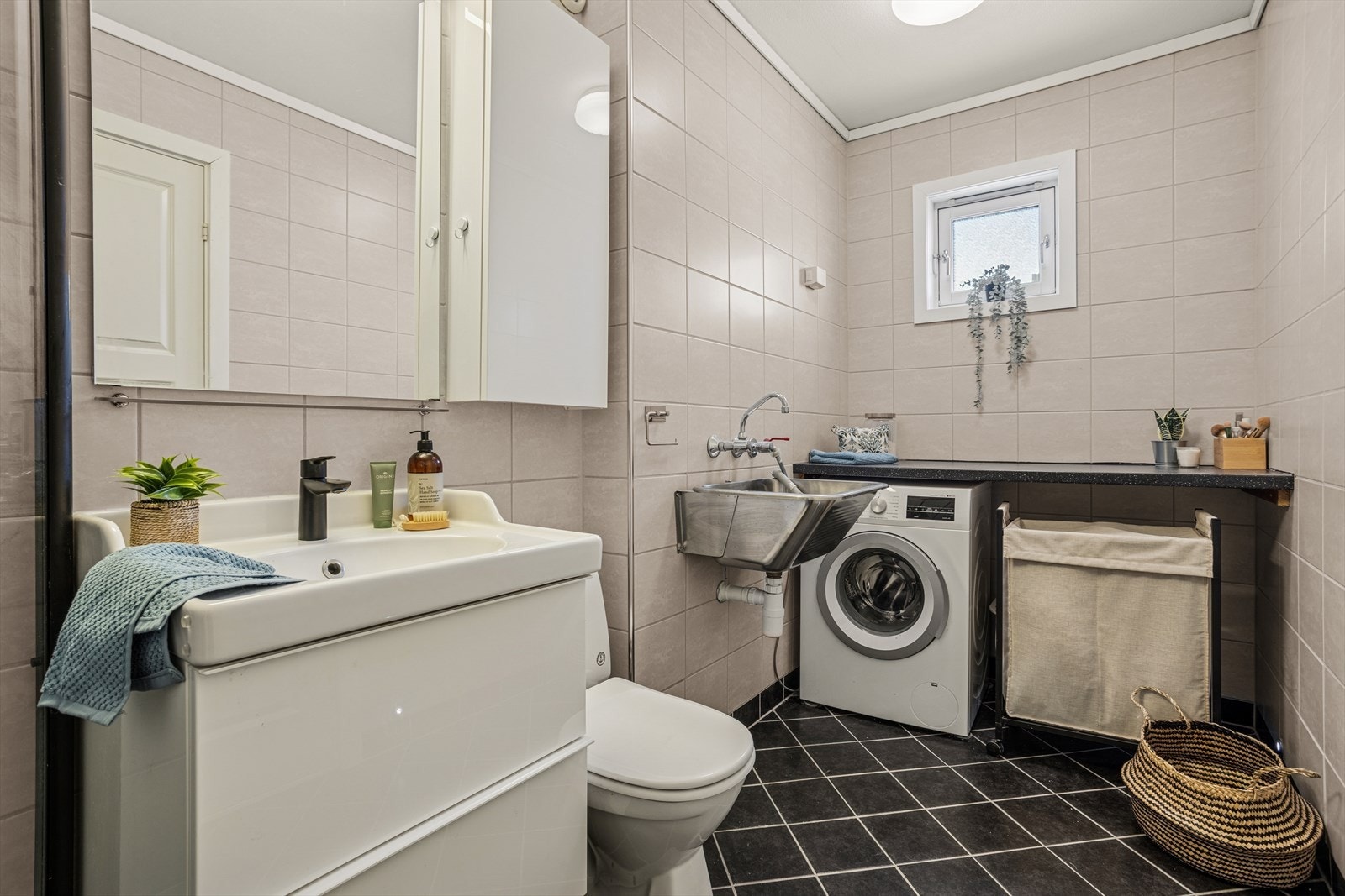 Baderommet er innredet med et benkeskap med nedfelt servant, speil med belysning, dusj med innfellbare dører og gulvmontert toalett. Her er også utslagsvask og praktisk benk med opplegg til vaskemaskin under. Galleribilde