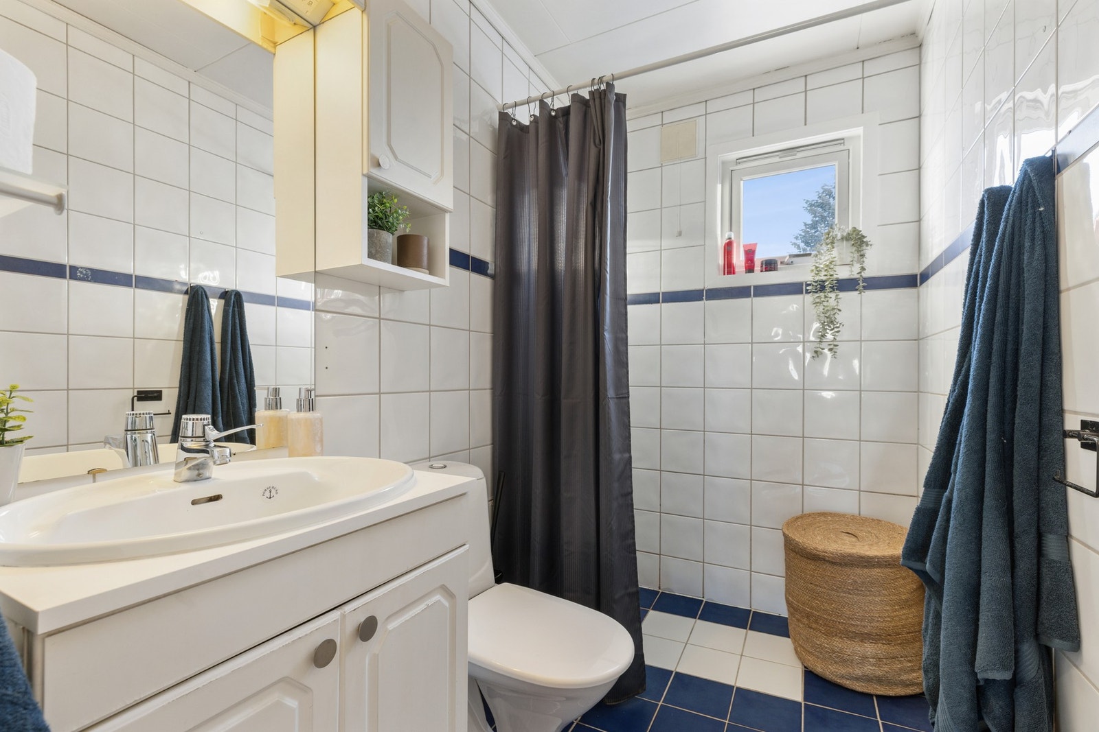 Dusjhjørne med forheng, dusjarmatur og hånddusj. Gulvmontert toalett. Vannrør av kobber. Synlige avløpsrør av plast og støpejern. Avtrekksventil i himling. Galleribilde