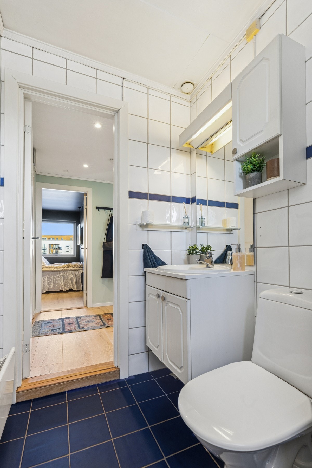 Baderom fra ukjent årstall. Flislagt gulv. Flislagte vegger. Malt himlingsflate. Vegghengt servantskap med nedfelt servant og ett-greps armatur. Speil med overlys, stikkontakt og skap over servant. Galleribilde