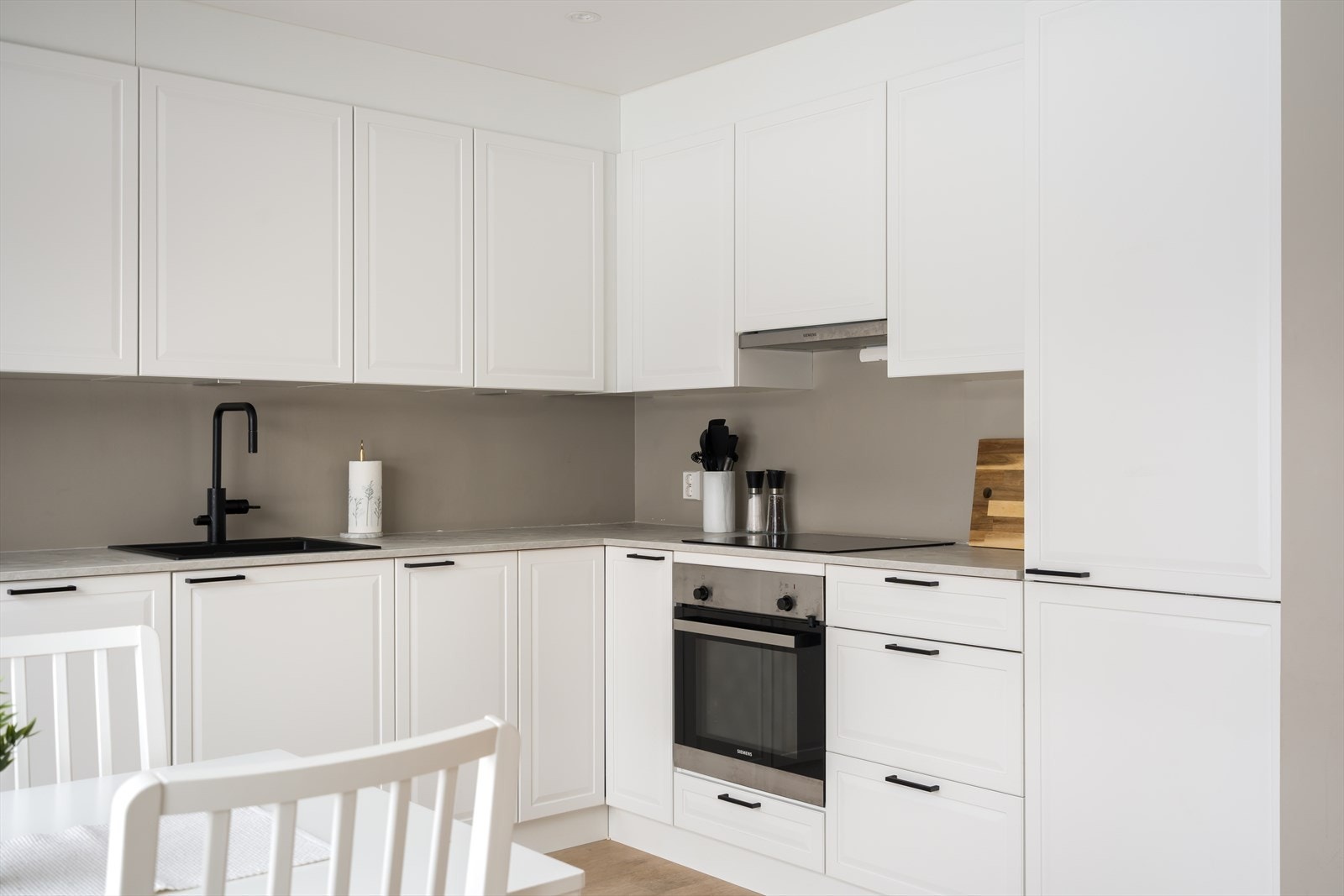 Innredningen har et tidløst uttrykk, med hvite, profilerte fronter, sort oppvaskkum og laminert benkeplate i lysegrått. Galleribilde