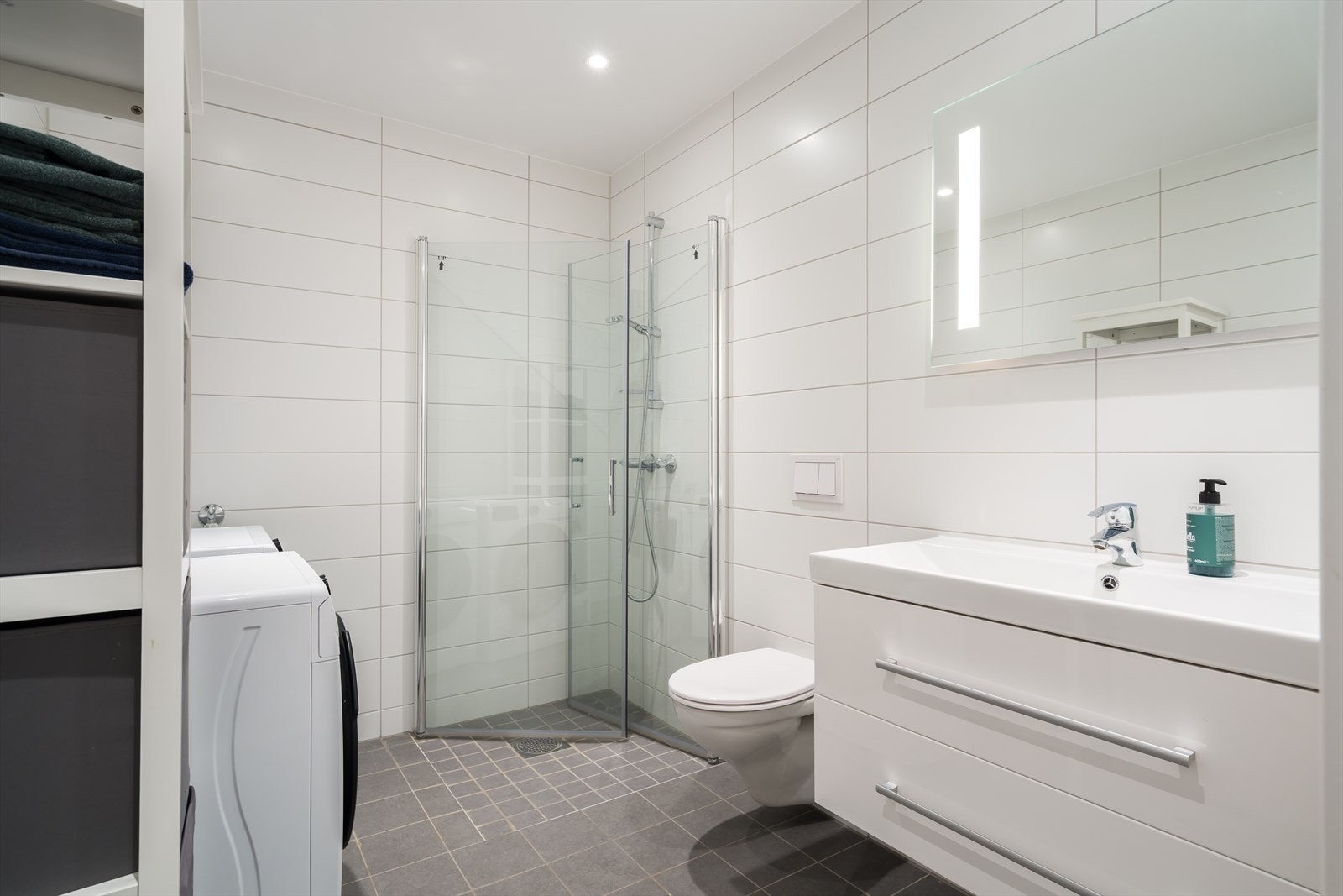 Hvite veggfliser kombineres med lysegrå gulvfliser for et delikat uttrykk. Galleribilde