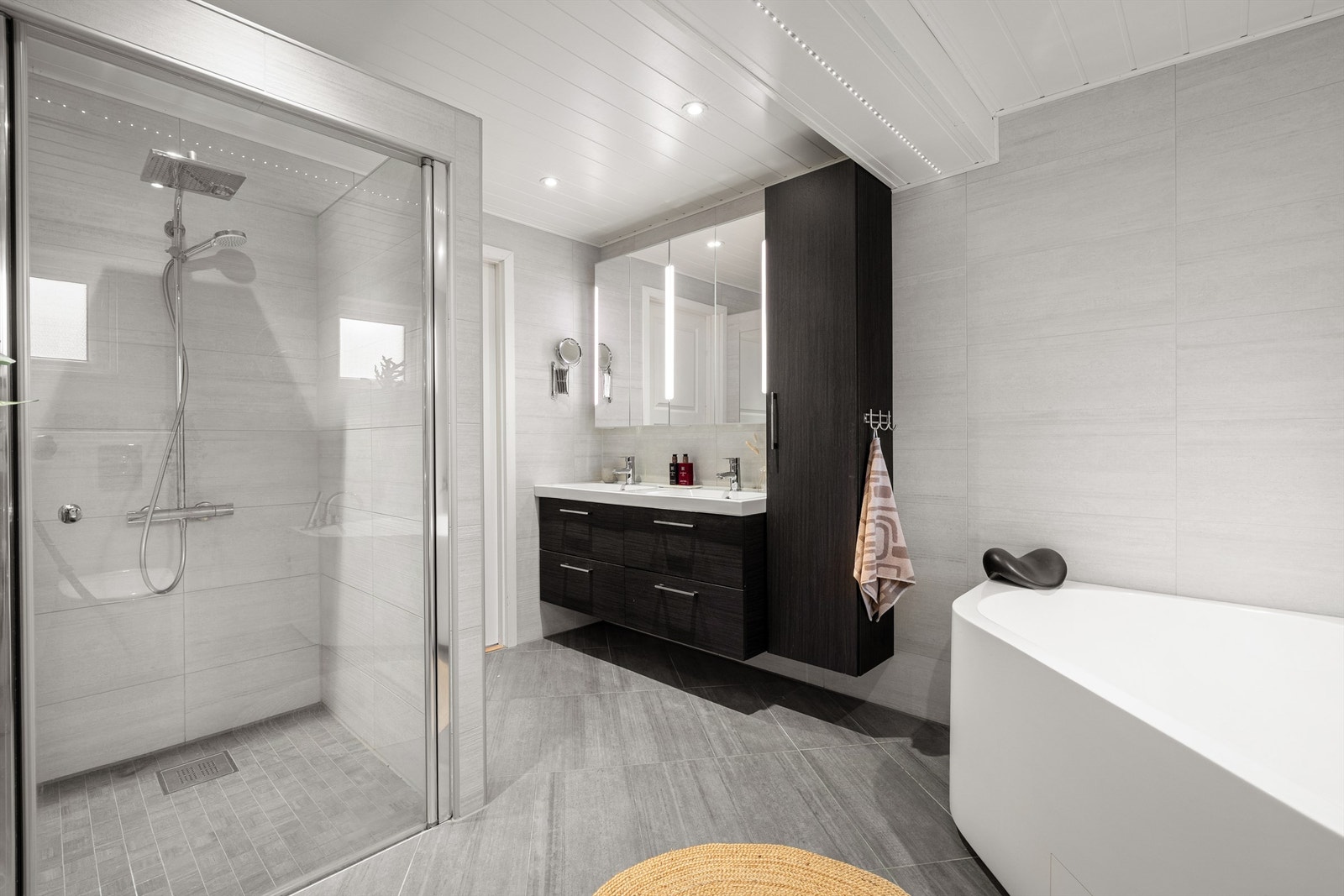 De mørke baderomsmøblene gir en fin kontrast til de lyse flisene. Med dobbelt servantoppsett og rikelig med oppbevaringsplass, er dette et baderom som dekker hele familiens behov. Galleribilde