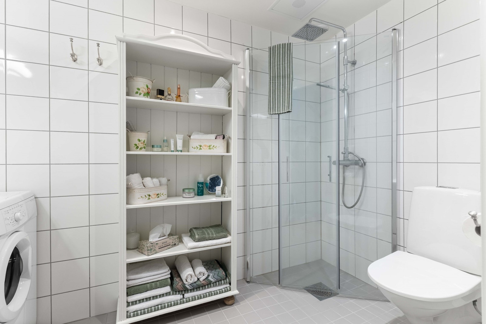 Lekkert dusjhjørne med innfellbare glassdører, dusjarmatur med hånddusj og regndusj. Vegghengt toalett og opplegg for vaskemaskin gir en praktisk og moderne løsning. Galleribilde