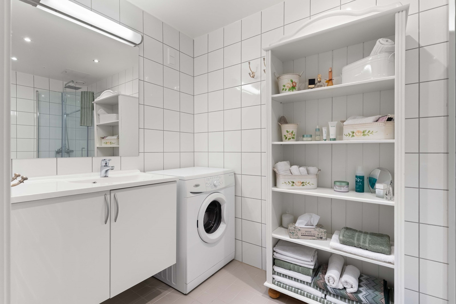 Flislagt bad med gulvvarme, flislagte vegger og downlights i himlingen. Moderne servantskap med heldekkende servant, ett-greps armatur og speil med belysning og stikkontakt over. Galleribilde