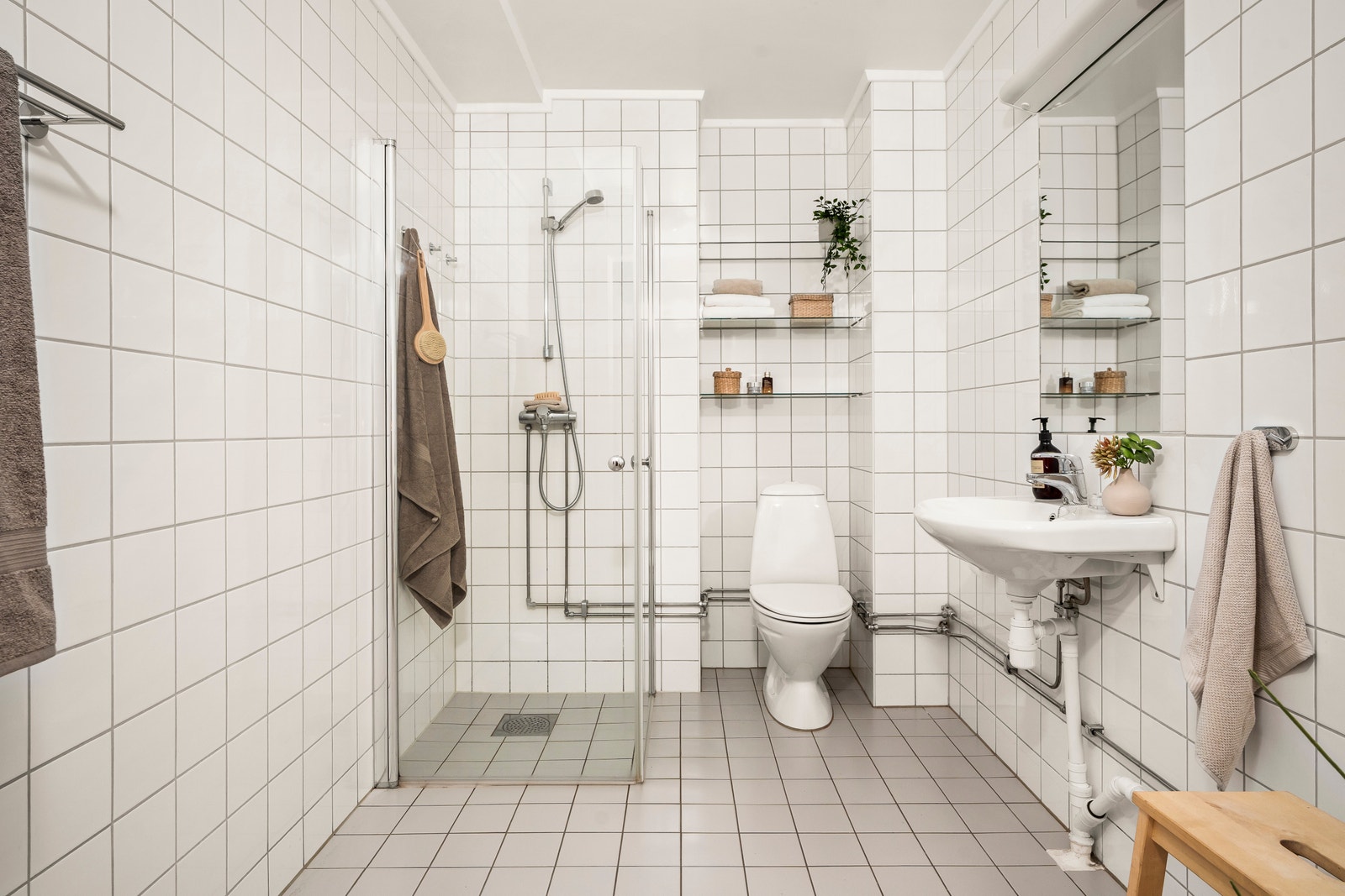 Stort, flislagt bad i lyse, moderne farger med opplegg for vaskemaskin, praktisk baderomsinnredning og dusjhjørne med glassdører. Galleribilde