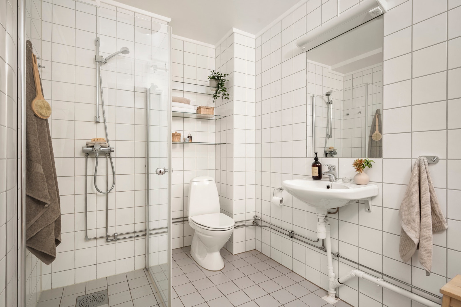 Stort, flislagt bad i lyse, moderne farger med opplegg for vaskemaskin, praktisk baderomsinnredning og dusjhjørne med glassdører. Galleribilde