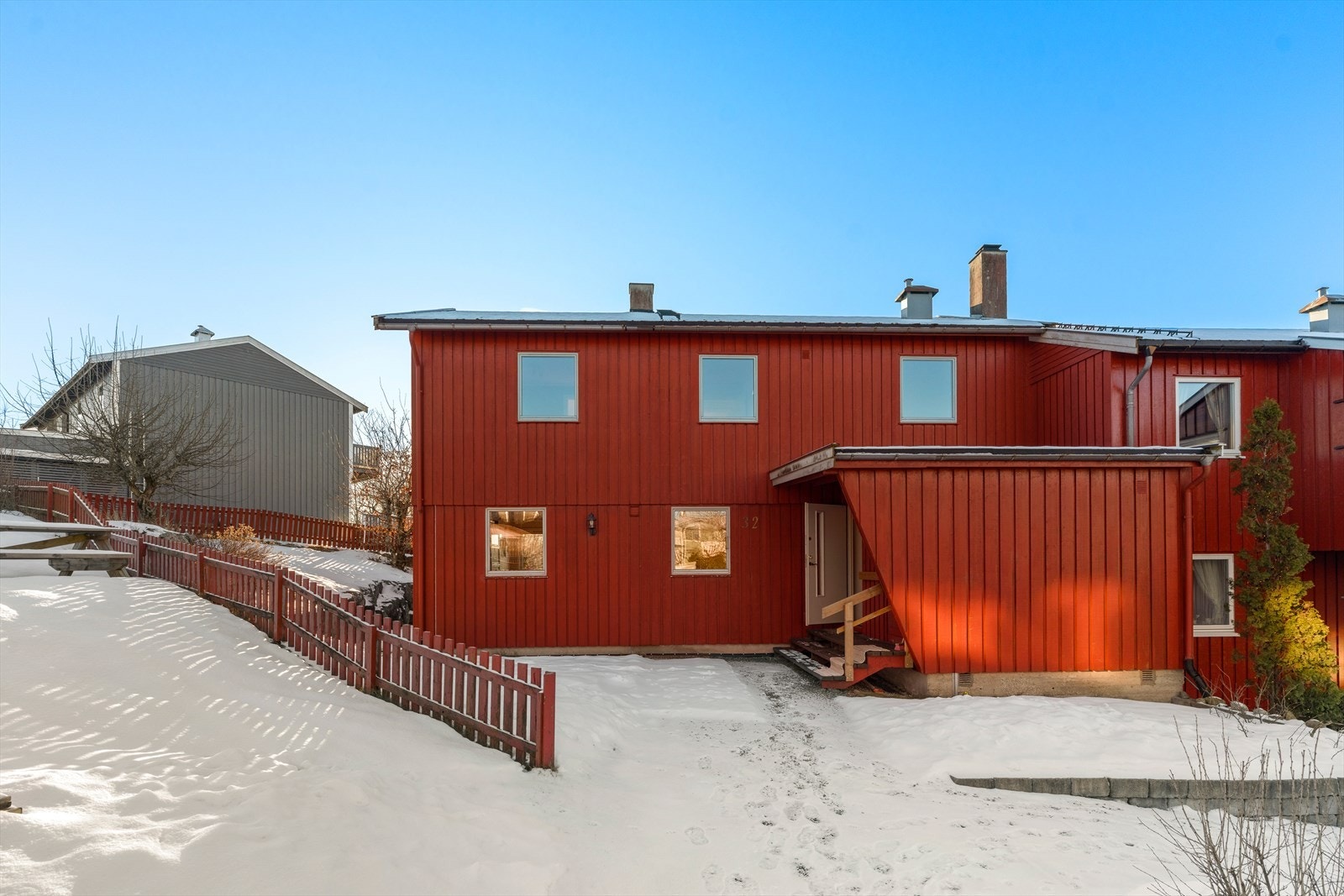 Enebolig med en klassisk fasade i rød trepanel og overbygget inngangsparti. Galleribilde