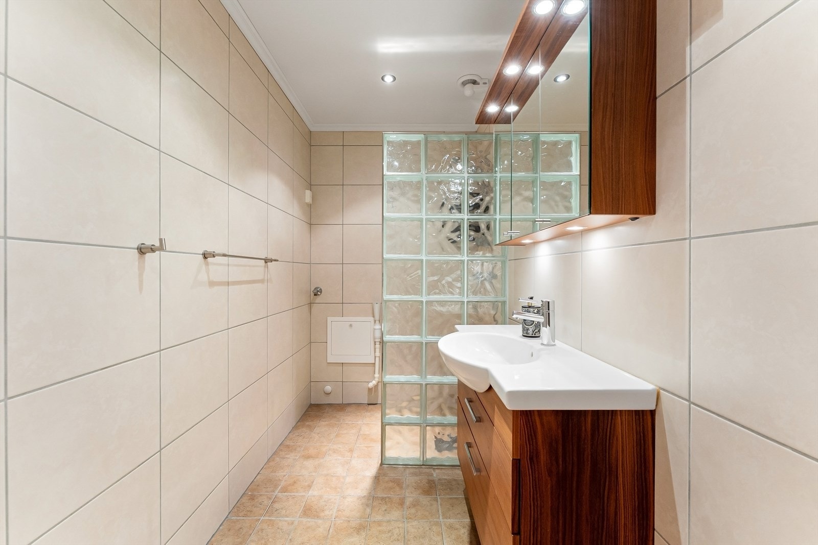 Badet har innredning med nedfelt servant, veggmontert toalett, dusjvegg i glassbyggerstein samt opplegg for vaskemaskin. Galleribilde