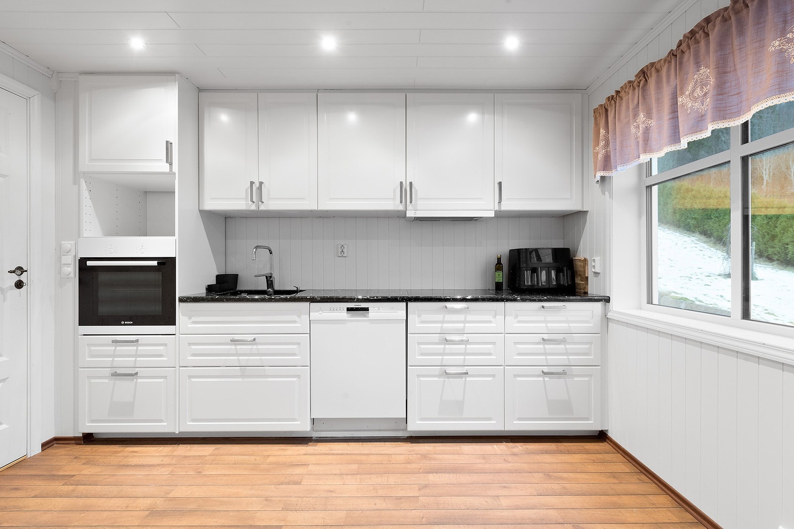 Lyst og innbydende kjøkken. Innredningen fra IKEA ble byttet i 2014. Profilerte malte fronter med polert steinplate som benkeplate. Galleribilde