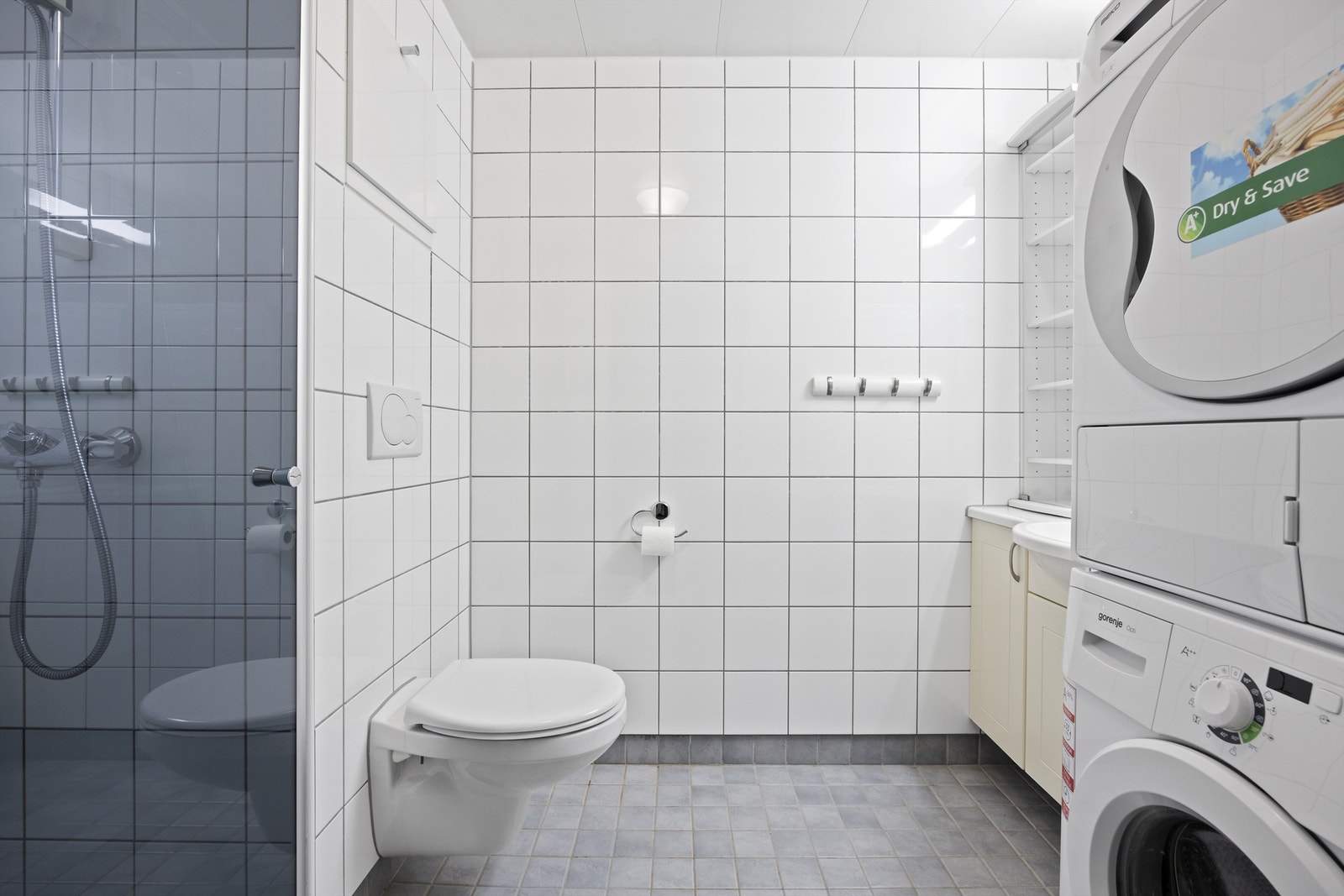 Romslig og flislagt bad med gulvvarme. Badet består av dusjnisje med glassdør, vegghengt toalett, heldekkendeservant oppå vegghengt servantskap og innmurt speil med lys over. Vaskemaskin og tørketrommel medfølger Galleribilde