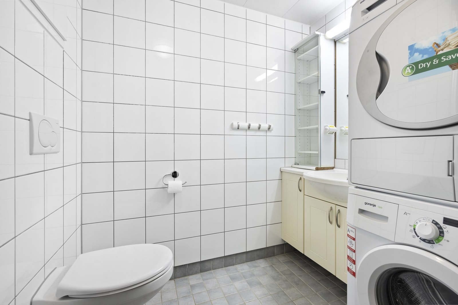 Romslig og flislagt bad med gulvvarme. Badet består av dusjnisje med glassdør, vegghengt toalett, heldekkendeservant oppå vegghengt servantskap og innmurt speil med lys over. Vaskemaskin og tørketrommel medfølger Galleribilde